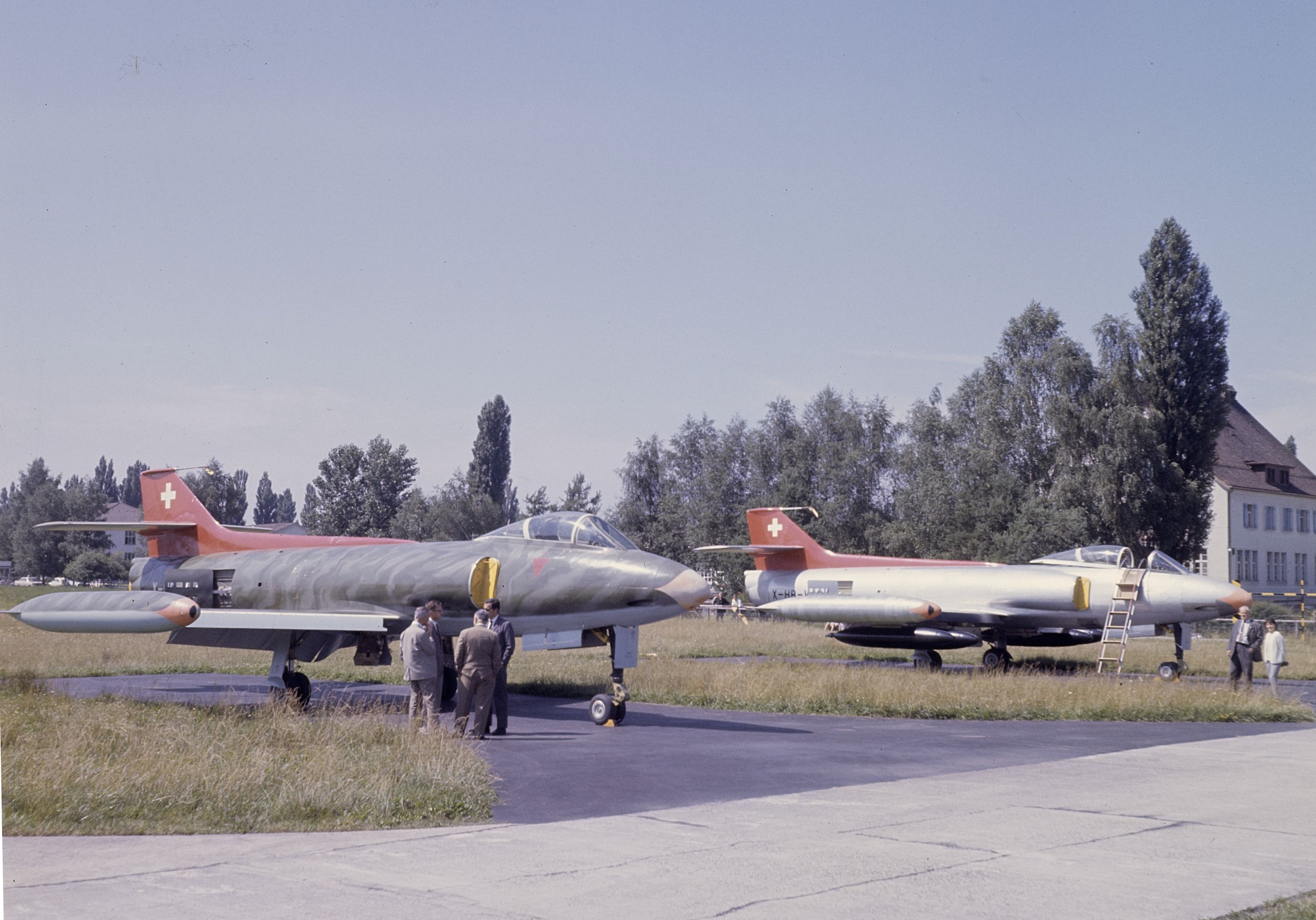 Two silver FFA P-16 prototypes with red Swiss tails, parked at Altenrhein beside a group of people.